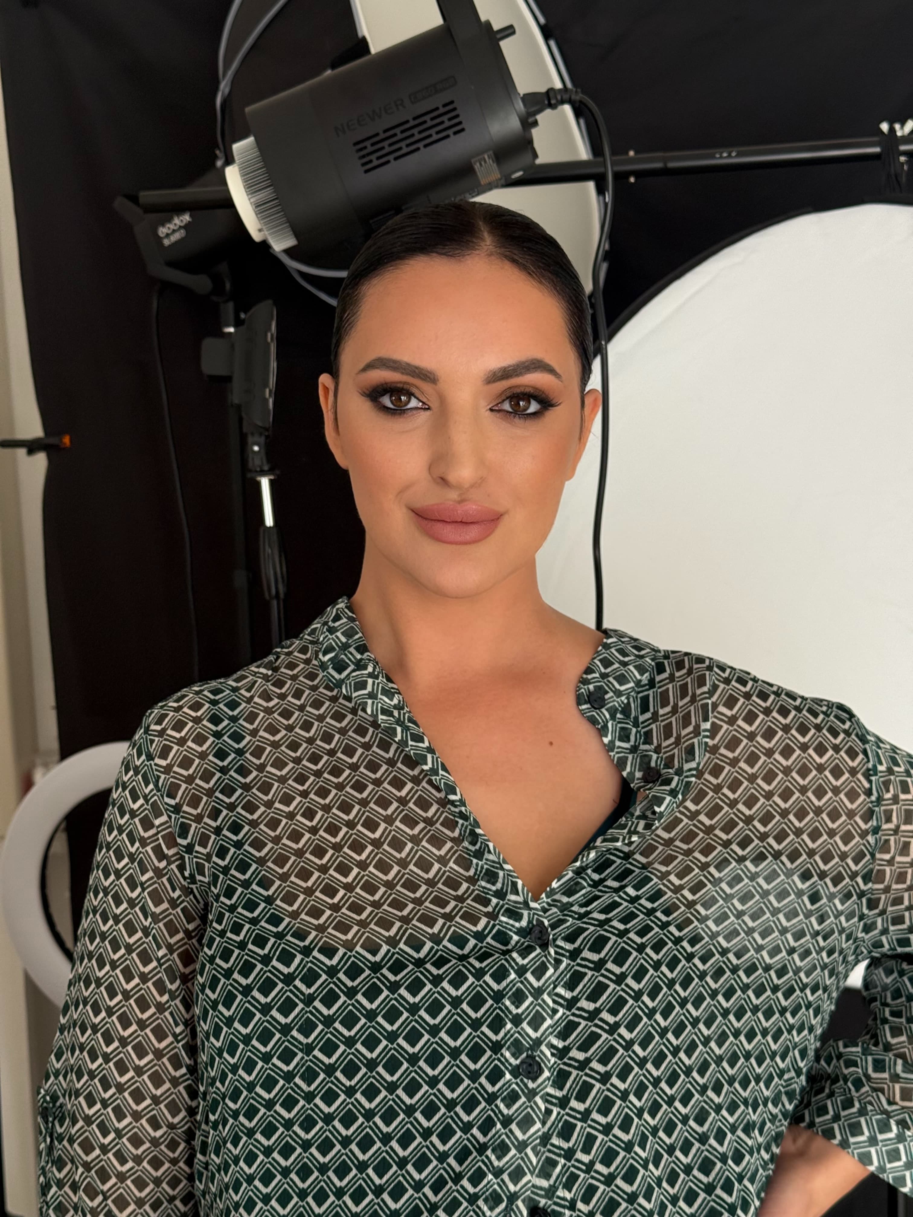 Woman with dark hair wearing a green geometric shirt in a professional photography studio.