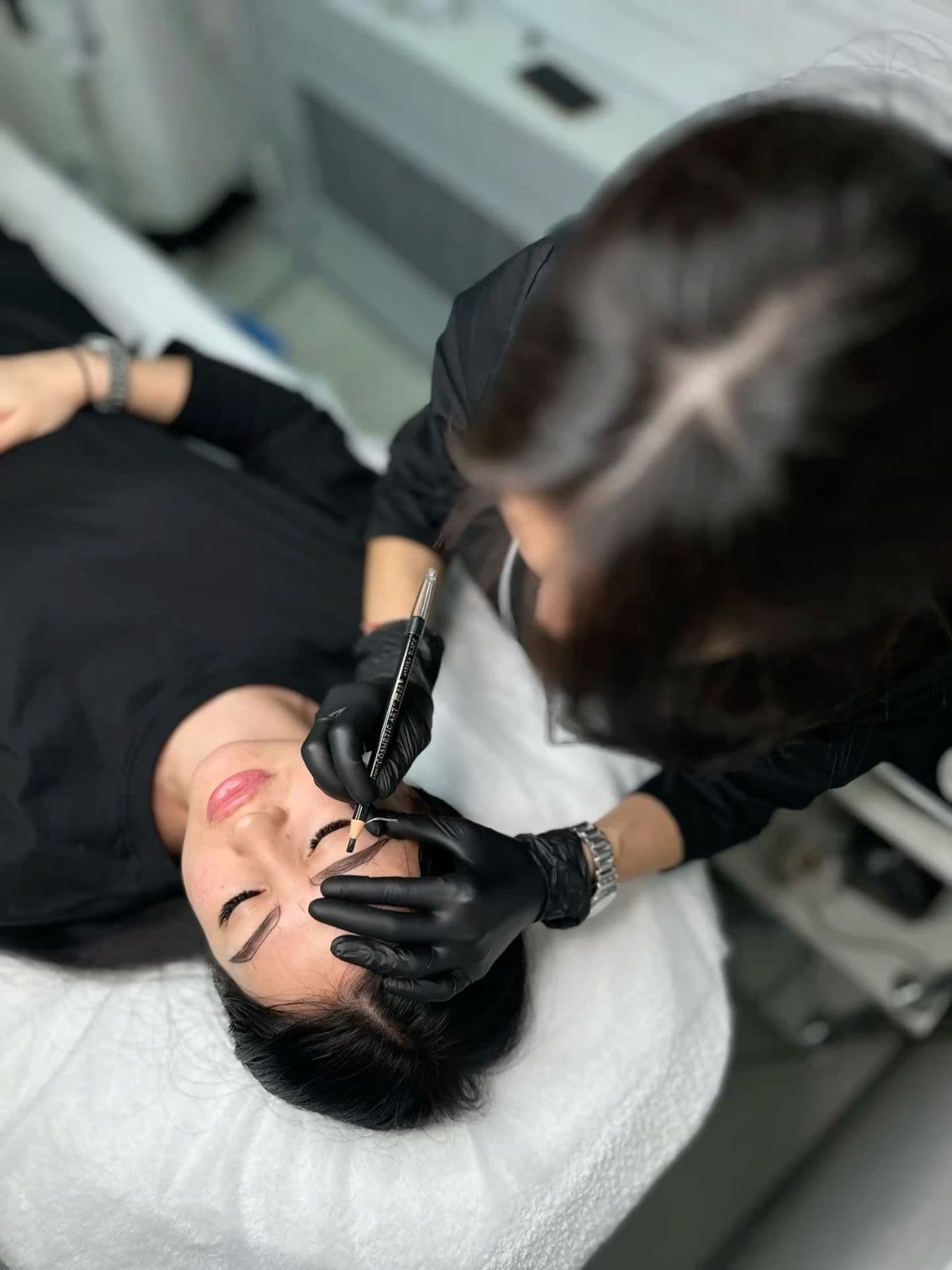 Professional technician mapping a client's eyebrows with a pencil during a permanent makeup procedure.